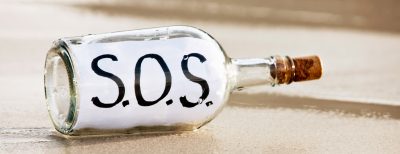 A bottle containing a desperate  message saying "SOS", presumably from a frantic castaway, is washed up on the shore and reflected in the sand.